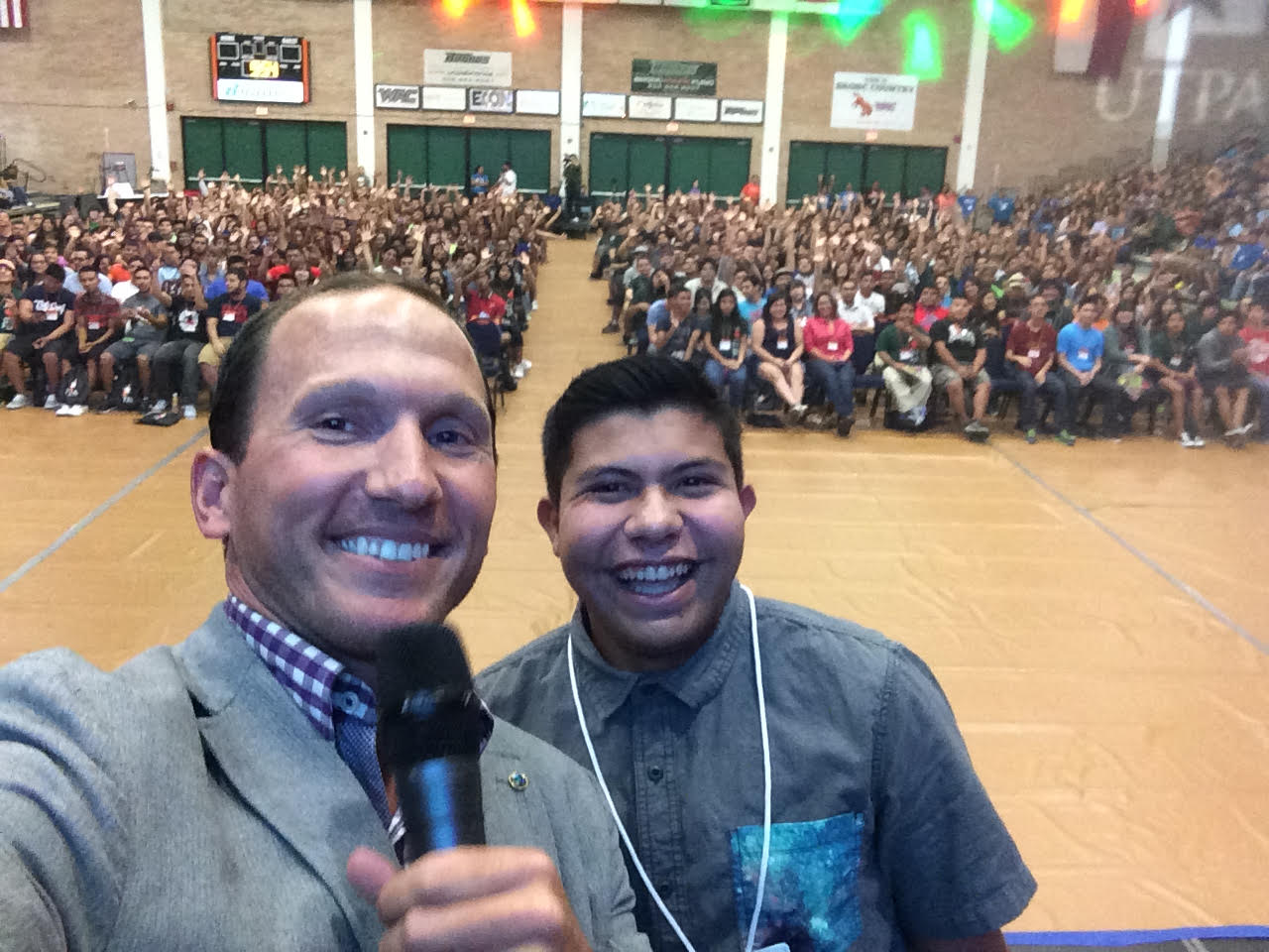Kevin with a student in front of a packed gymnasium audience
